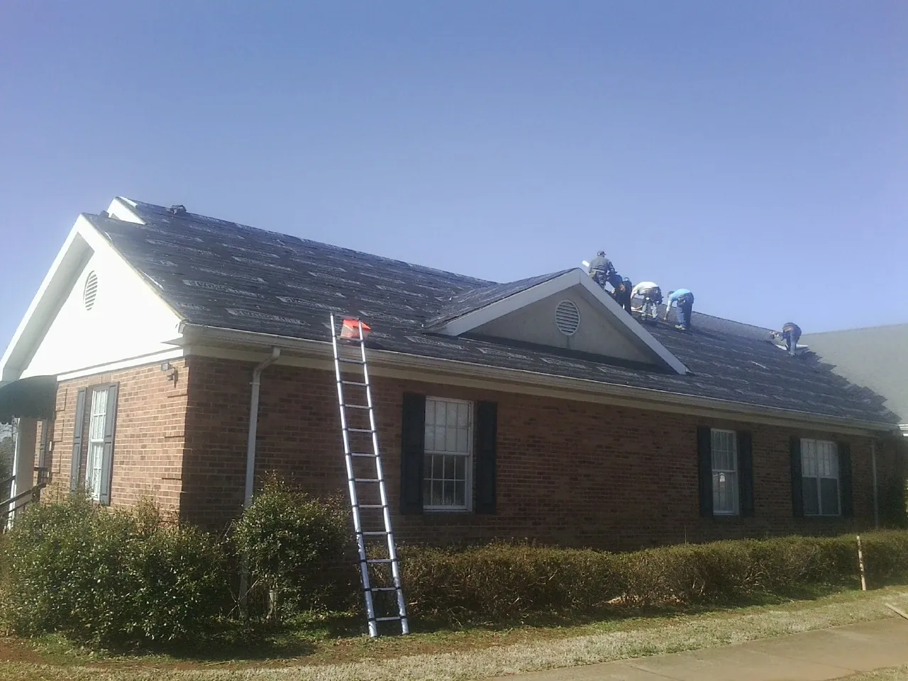 Crew tearing shingles off a brick ranch roof with a ladder set — Emergency Roof Repair work by our crew in Singers Glen
