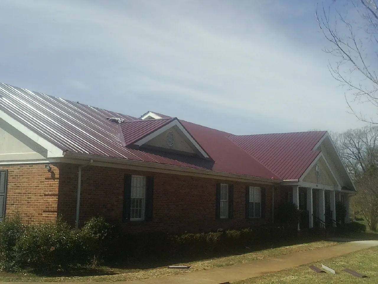 Red metal roof with gabled entries on a long brick building, from a Hail Damage Roof Repair job in Singers Glen