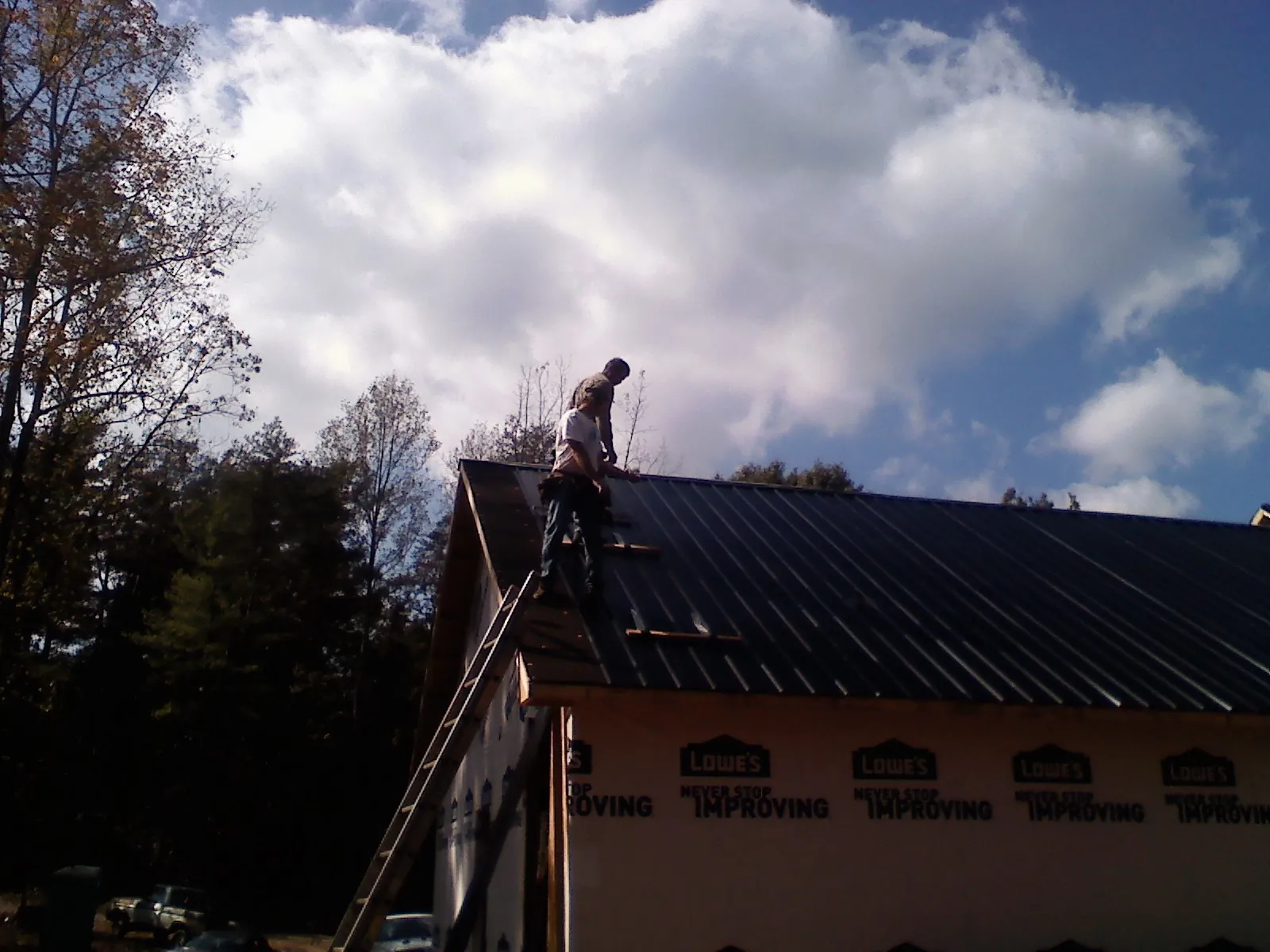 Roofer fastening dark metal panels high against a cloudy sky, from a Roof Inspection job in Singers Glen