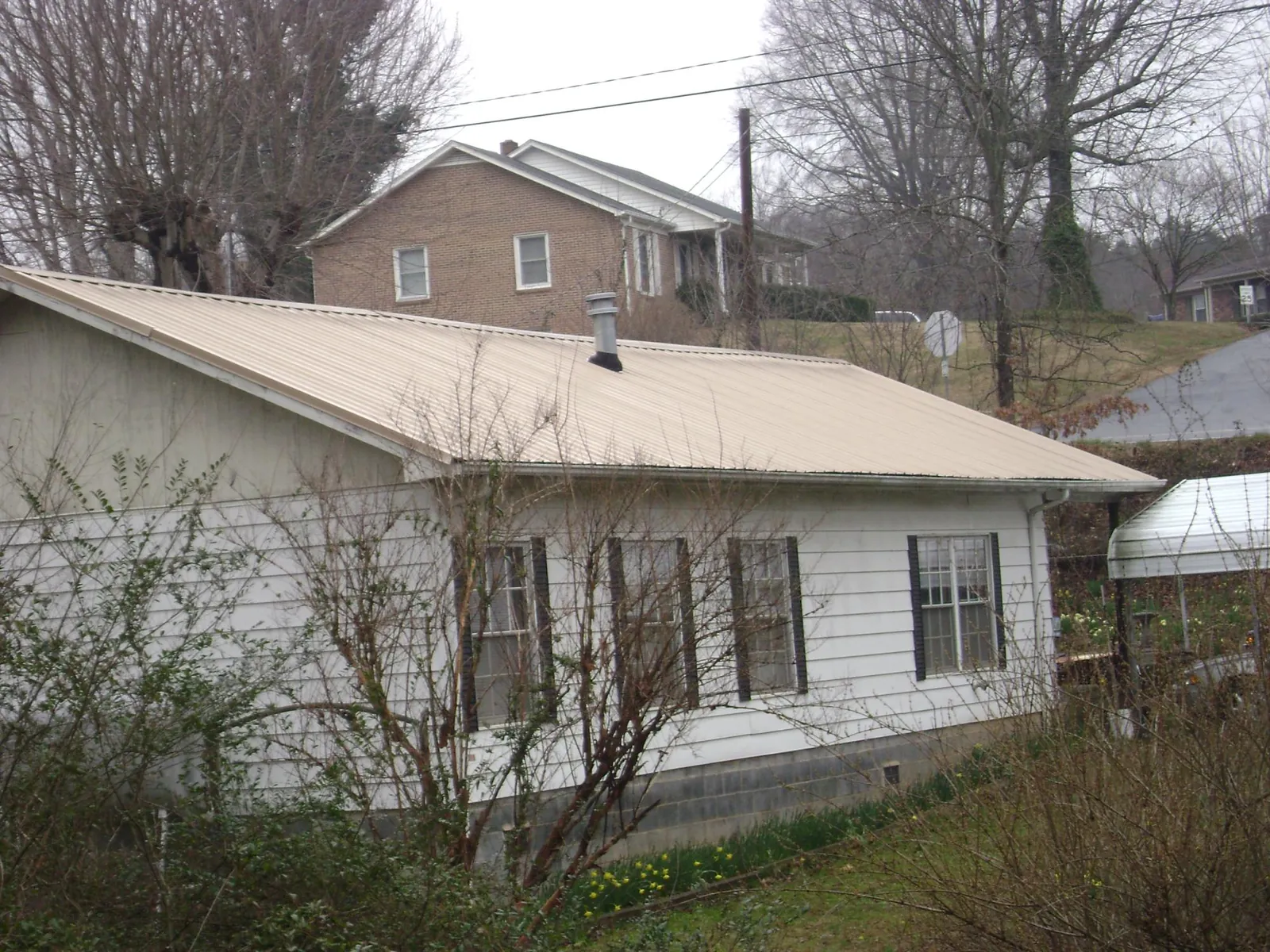 Tan metal roof on a white sided house set into a hillside — Commercial Roofing by Roofing Brothers in Singers Glen